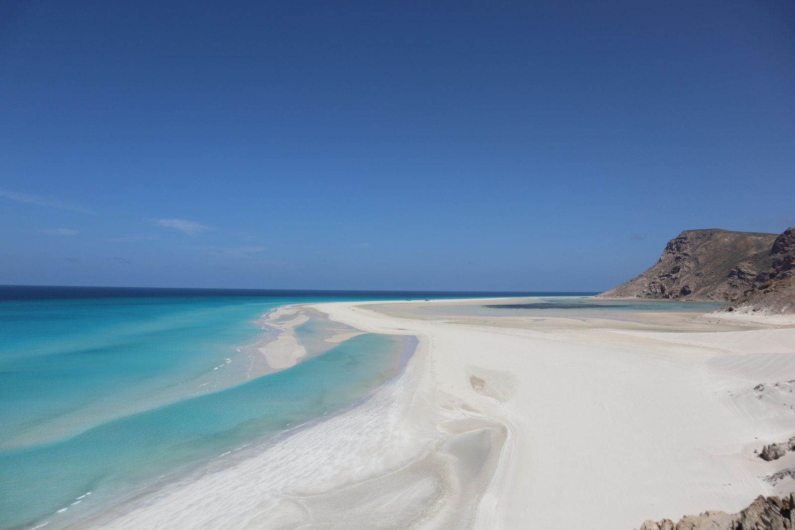 Turquoise ocean meets white sand beach with rocky hills.