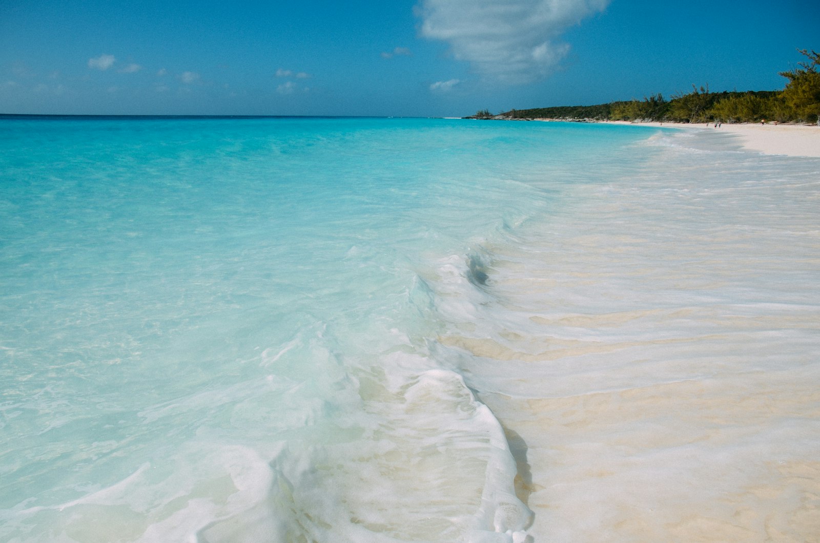 Turquoise ocean waves gently lap a white sand beach.