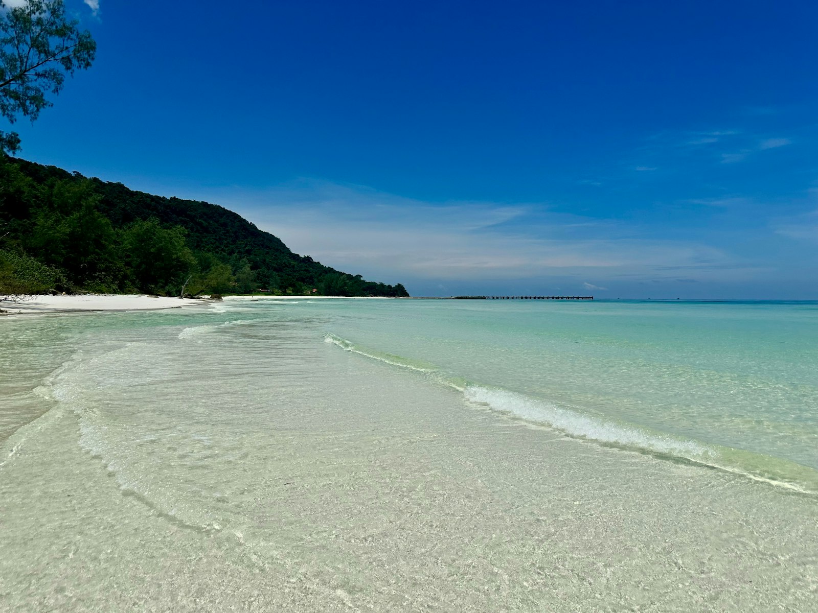 A sandy beach with clear blue water and a hill in the distance